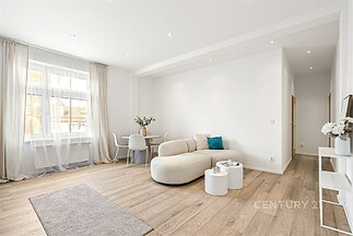 Světlý obývací pokoj s moderním designem, parketová podlaha a velká okna, které zajišťují dostatek přirozeného světla, nabízí komfortní bydlení.