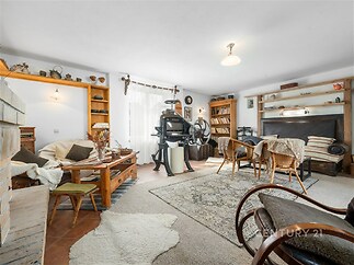 Světlý obývací pokoj s dřevěným nábytkem, velkými okny a parketovou podlahou, zařízený v útulném rustikálním stylu vybavený knihovnou.