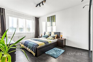 Prostorná ložnice s moderními dlažbami, velkými okny a elegantním nábytkem, poskytující světlý a vzdušný interiér.