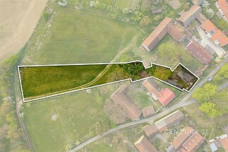 Pozemek v klidné lokalitě s travnatou plochou a vzrostlými stromy, ideální pro stavbu rodinného domu, obklopený přírodou a blízko infrastruktury.