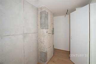 Moderní interiér s betonovou stěnou, parketovou podlahou a minimalistickým osvětlením. Světlé odstíny zvyšují dojem prostornosti.