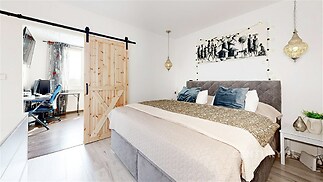 Prostorná ložnice s moderními prvky, parketová podlaha, stylové závěsné osvětlení, posuvné dřevěné dveře vedoucí do pracovny