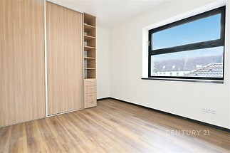 Pokoj s vestavěnými skříněmi, moderní parketová podlaha a velké okno poskytující dostatek denního světla.