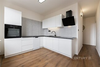 Moderní kuchyň s bílými skříňkami, parketovou podlahou a stylovými dlaždicemi na stěně, poskytující světlý a elegantní prostor