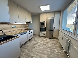 Moderní kuchyň s laminátovou podlahou, vestavěné spotřebiče a velká okna nabízejí světlý prostor vhodný pro rodinné vaření