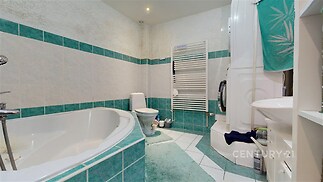 Koupelna s rohovou vanou, bílomodrá dlažba, moderní design, s vyhřívaným žebrovým radiátorem, světlý interiér.
