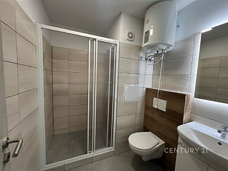 Moderní koupelna s dlažbou, sprchovým koutem a závěsnou toaletou, světlé obklady a elektrický bojler, vynikající stav.