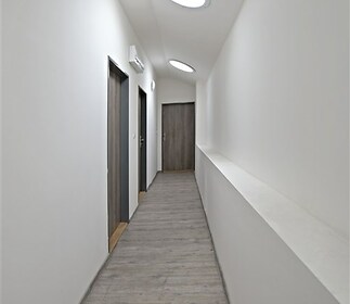 Dlouhá chodba s moderními dřevěnými dveřmi, světlou parketovou podlahou a stropními světlíky, které zajišťují přirozené osvětlení.