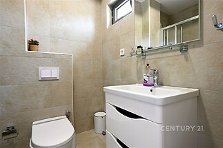Koupelna s moderními dlaždicemi, světlé barvy, závěsné WC, velké zrcadlo, praktická skříňka pod umyvadlem.