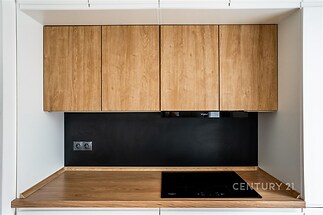 Moderní kuchyň s dřevěnými skříňkami, indukční varnou deskou a černým obkladem. Elegantní povrch a kvalitní materiály.
