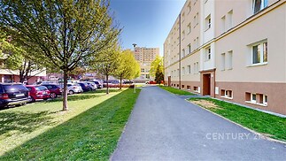 Pěší cesta před bytovým domem s upravenou zelení, moderní revitalizace fasády, blízkost městské infrastruktury, klidná lokalita.