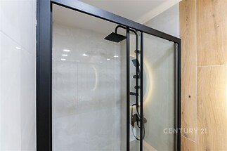 Moderní koupelna s elegantními skleněnými dveřmi, černými kovovými rámy a stylovou sprchovou hlavicí, dlažba s přírodním dřevěným dekorem