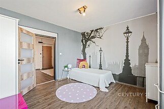 Dětský pokoj s dřevěnou podlahou, velkou nástěnnou tapetou s motivem města a minimalistickým nábytkem, světlý a moderní prostor.