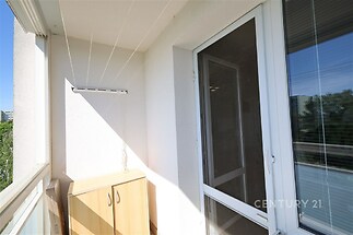 Zasklený balkon s dlažbou a úložnou skříní, poskytuje výhled na zeleň, ideální pro relaxaci díky zajištění soukromí a světlému designu.