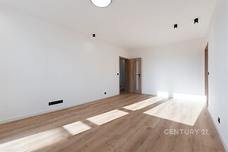 Světlý obývací pokoj s parketovou podlahou, moderní osvětlení, velká okna poskytující dostatek přirozeného světla, nedávno rekonstruovaný prostor.