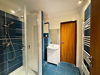 Moderní koupelna s modrou dlažbou, sprchovým koutem a elegantními obklady, vybavená topným žebříkem a dřevěnými dveřmi, světlá a útulná.