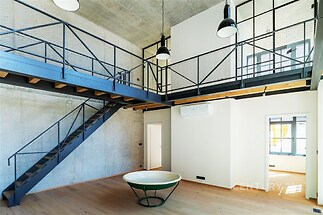 Industriální obývací pokoj s parketovou podlahou, kovovým schodištěm a vysokými stropy, moderní design a velká okna přináší světlost.