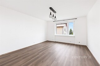 Světlý obývací pokoj s novou parketovou podlahou, velká okna zajišťující dostatek přirozeného světla, moderní osvětlovací tělesa na stropě