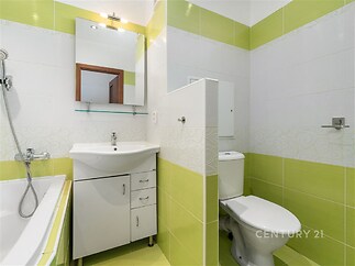 Koupelna s bílou keramickou dlažbou a svěžími zelenými obklady, obsahuje moderní umyvadlo se skříňkou a sanitární zařízení v dobrém stavu.