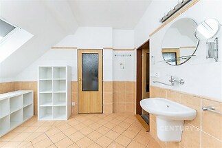 Prostorná koupelna s dlažbou, skleněné sprchové dveře, bílá sanitární keramika a úložné police, moderní a světlé provedení.