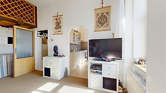 Světlý obývací pokoj s velkými okny, parketovou podlahou a moderním nábytkem. Prostor je propojený s kuchyní pomocí obloukového průchodu.