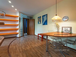 Jídelní kout s parketovou podlahou, moderní skleněný stůl a vestavěné police, světlé zdi zdobené uměním, stylové osvětlení pro útulný vzhled.