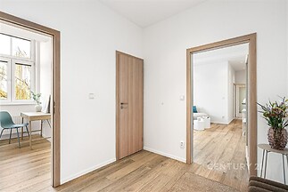 Chodba s parketovou podlahou a moderním dřevěným obložením, propojuje světlé pokoje s velkými okny a elegantním nábytkem.