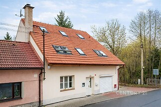 Fasáda rodinného domu s červenou střechou a střešními okny, vedle přilehlého lesa, moderní stavba v klidné lokalitě.