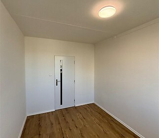 Prázdná místnost s parketovou podlahou, bílými stěnami a moderním osvětlením, ideální pro přizpůsobení interiéru.