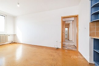 Světlý obývací pokoj s korkovou podlahou a velkými okny, moderní vzhled, poblíž vstupu do kuchyně s dlažbou.