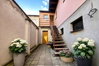 Venkovní dvůr s dlažbou, dřevěným schodištěm a květináči. Světlé stěny dodávají prostoru moderní vzhled.