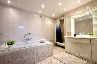 Prostorná koupelna s moderní dlažbou, vestavěným sprchovým koutem a světlým zrcadlovým kabinetem poskytuje elegantní vzhled.