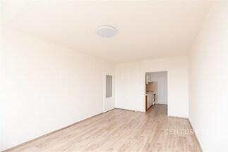 Světlý obývací pokoj s dřevěnou podlahou, velká okna a moderní bílá výmalba nabízejí příležitost pro útulné bydlení v nově rekonstruovaném bytě.