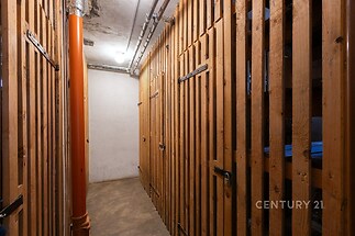 Úložný prostor s dřevěnými latěmi, betonová podlaha a základní osvětlení. Ideální pro skladování, v dobrém stavu.