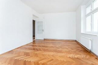 Světlý obývací pokoj s parketovou podlahou, velká okna zajišťují dostatek přirozeného světla, moderní bílý interiér