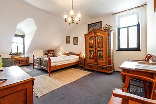 Prostorná ložnice s tmavým kobercem, dřevěným nábytkem ve venkovském stylu a velkými okny, která poskytují dostatek přirozeného světla.