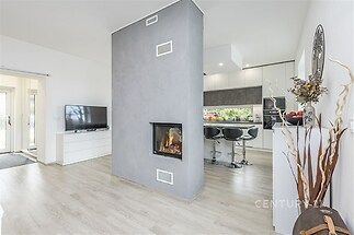Moderní obývací pokoj s krbovými kamny, parketovou podlahou a světlým interiérem, propojený s kuchyní s moderními spotřebiči.