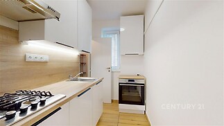 Moderní kuchyň s vestavěnými spotřebiči, dřevěnou pracovní deskou a světlými skříňkami, dlažba na podlaze, ideální pro efektivní vaření.