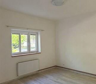 Světlý pokoj s laminátovou podlahou, velká okna a bílými stěnami. Okno poskytuje výhled do zahrady, ideální pro moderní bydlení.