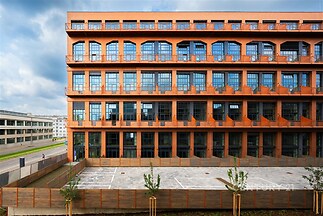 Fasáda moderního kancelářského komplexu s velkými okny, průmyslový design, cihlové prvky a venkovní dlažbou na parkovišti.