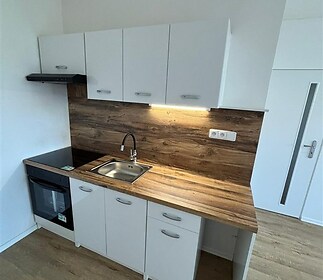 Moderní kuchyň s dřevěnou pracovní deskou, bílými skříňkami a parketovou podlahou. Vyniká kompaktním designem a kvalitními materiály.