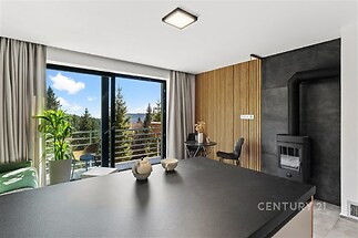 Moderní obývací pokoj s krbovými kamny, velkými okny a dřevěnou parketovou podlahou nabízí nádherný výhled na les a balkon pro relaxaci.