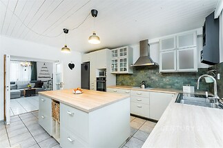 Moderní kuchyň s dlažbou, světlá s velkým ostrůvkem a vestavěnými spotřebiči. Stylové osvětlení a dostatek úložného prostoru, propojená s obývacím pokojem.