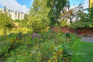 Zahrada s rozkvetlými květinami a vzrostlými stromy, cihlová zídka, útulná atmosféra, ideální pro relaxaci a venkovní aktivity.
