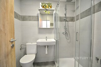 Moderní koupelna s dlažbou, sprchový kout a zrcadlová skříňka, světlé obklady, elegantní design.