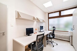 Kancelářský prostor s moderním vybavením, velká okna, světlé stěny a podlaha z dlažby, ideální pro produktivní pracovní prostředí.