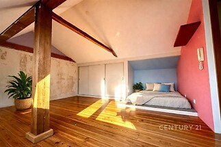 Podkrovní ložnice s dřevěnou podlahou, výmalbou růžové stěny a šikmým stropem. Velká okna zajišťují světlý a příjemný prostor.