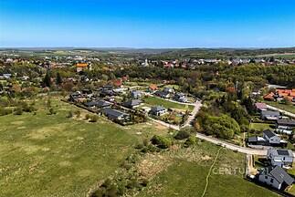 Letecký pohled na klidnou rezidenční oblast s moderními rodinnými domy, velkou zahradou a okolní zelení, ideální pro rodinné bydlení.