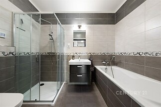 Moderní koupelna s dlažbou, proskleným sprchovým koutem a vestavěnou vanou, elegantní design a kvalitní materiály pro komfortní bydlení.