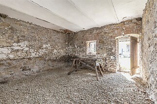 Rustikální místnost s kamennými zdmi, přírodním povrchem podlahy a otevřenými dveřmi poskytujícími přirozené světlo, ideální pro rekonstrukci.